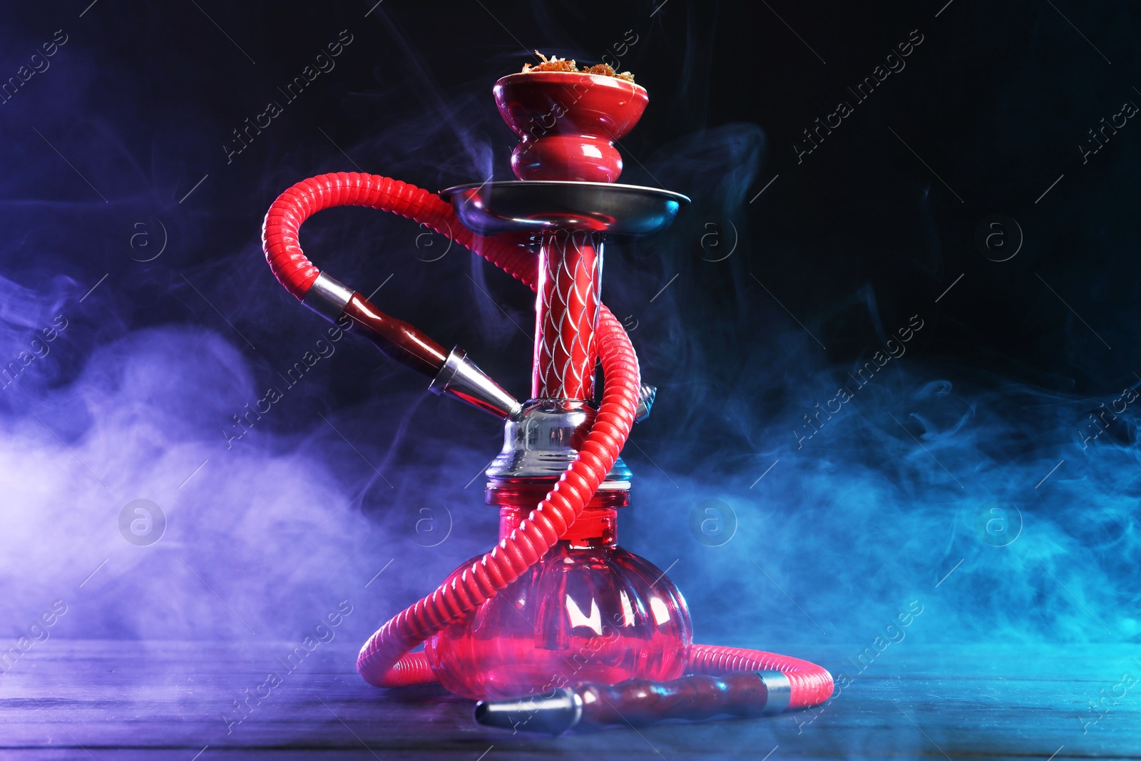 Hookah on wooden table with smoke in color lights against black background Photo of Hookah on wooden table with smoke in color lights against black background