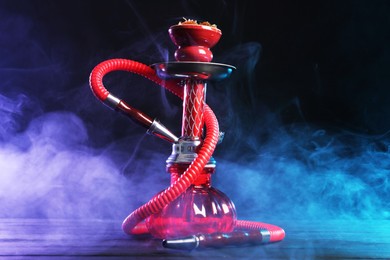 Photo of Hookah on wooden table with smoke in color lights against black background