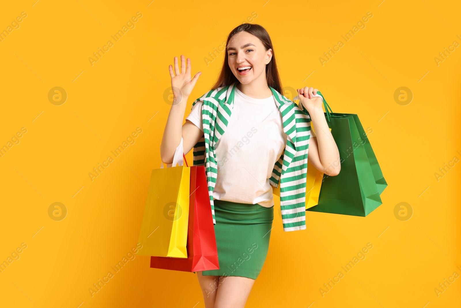 Positive woman with shopping bags waving on yellow background Photo of Positive woman with shopping bags waving on yellow background