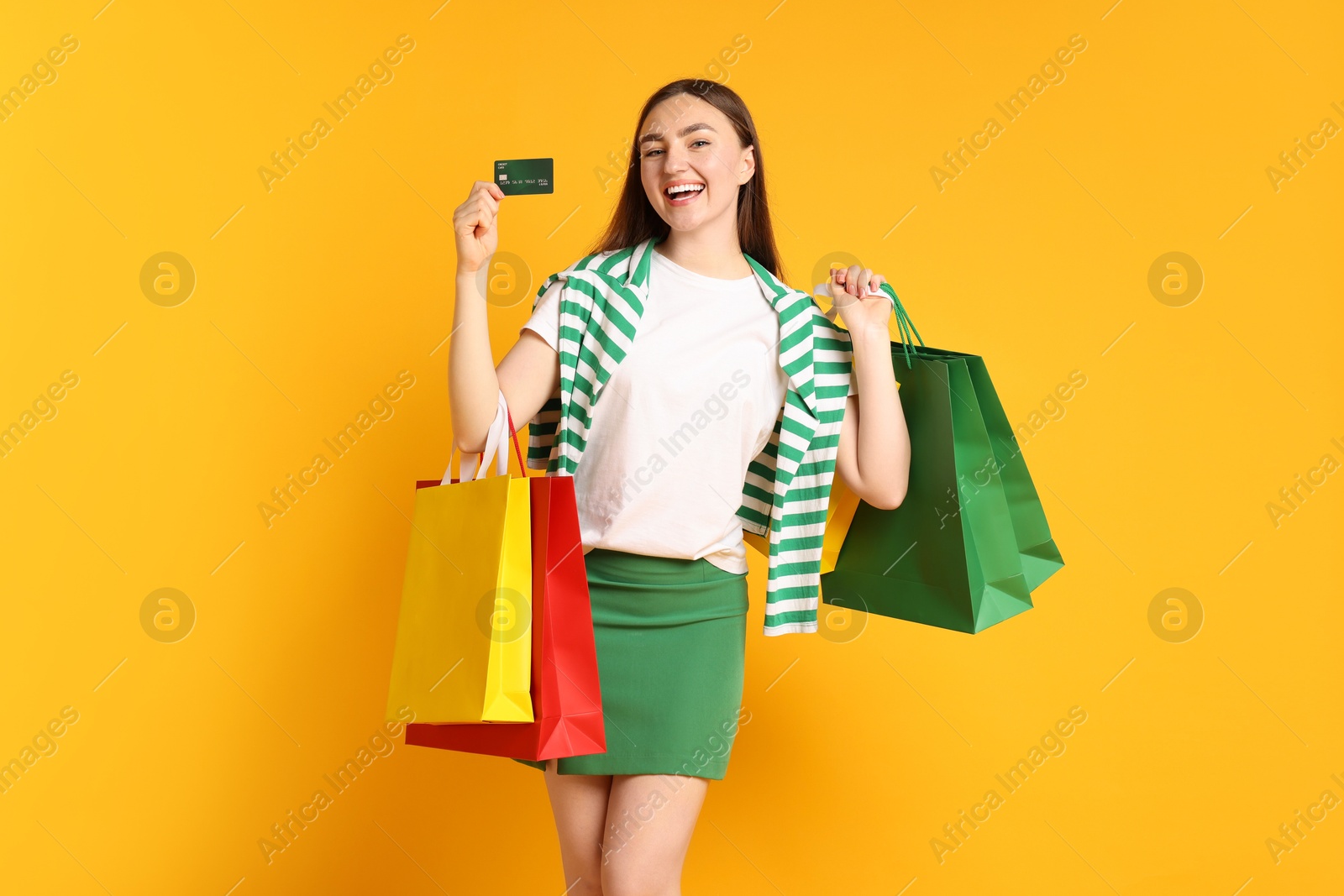 Positive woman with credit card and shopping bags on yellow background Photo of Positive woman with credit card and shopping bags on yellow background