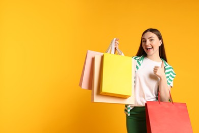 Photo of Excited woman with shopping bags showing thumbs up on yellow background. Space for text