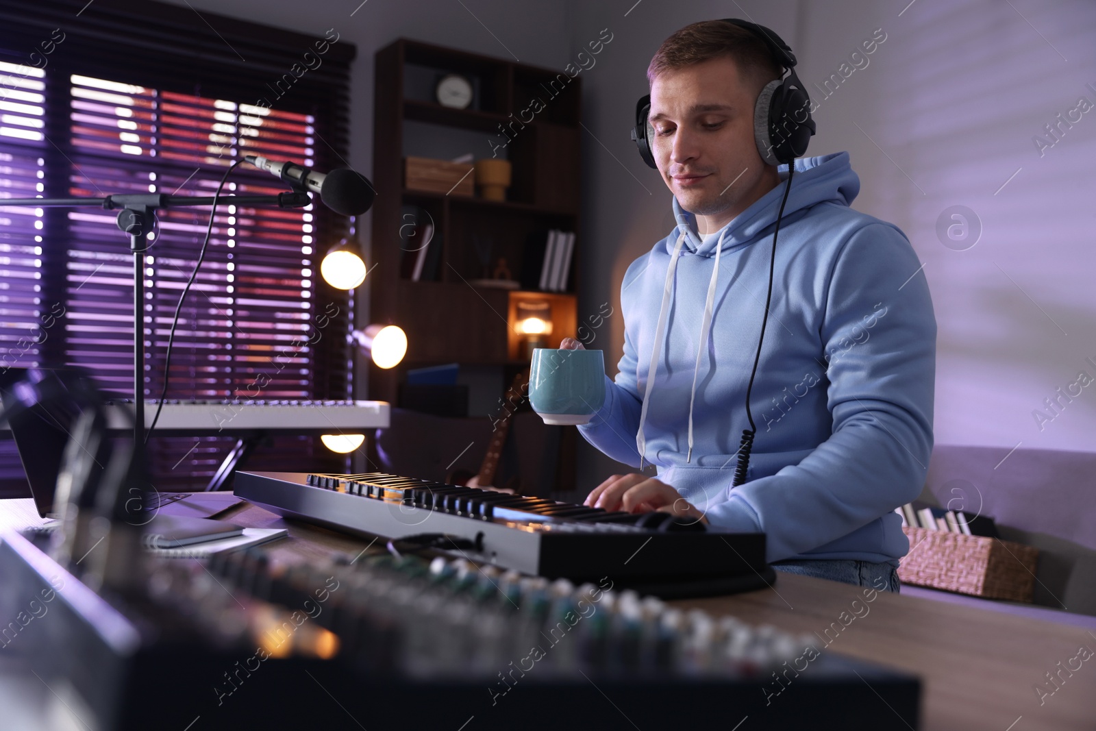 Man in headphones working with MIDI keyboard at table in home studio, low angle view Photo of Man in headphones working with MIDI keyboard at table in home studio, low angle view