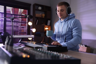 Photo of Man in headphones working with MIDI keyboard at table in home studio, low angle view