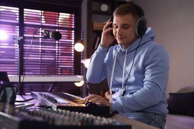 Photo of Man in headphones working with MIDI keyboard at table in home studio