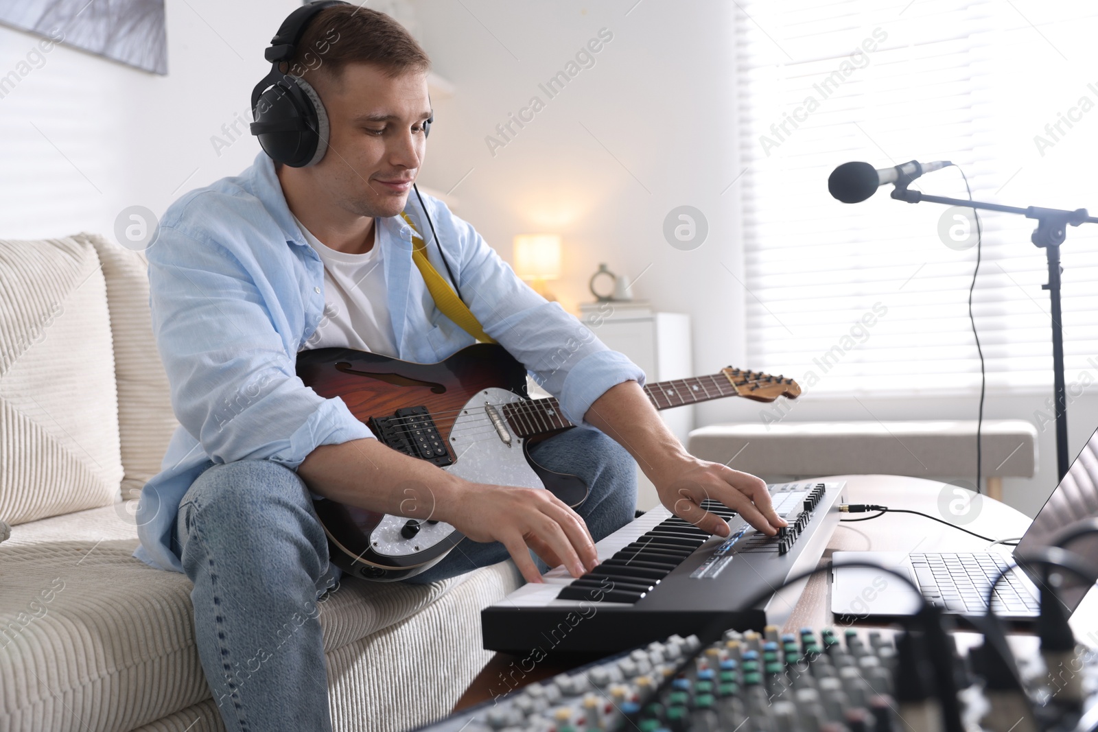 Man in headphones working with MIDI keyboard and guitar at table in home studio Photo of Man in headphones working with MIDI keyboard and guitar at table in home studio
