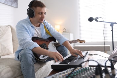 Photo of Man in headphones working with MIDI keyboard and guitar at table in home studio