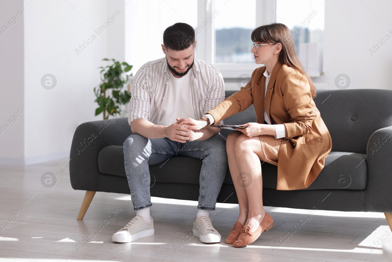 Photo of Psychologist supporting patient during therapy session on sofa in office