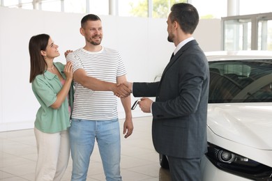 Photo of Salesman shaking hands with happy family near new car in salon