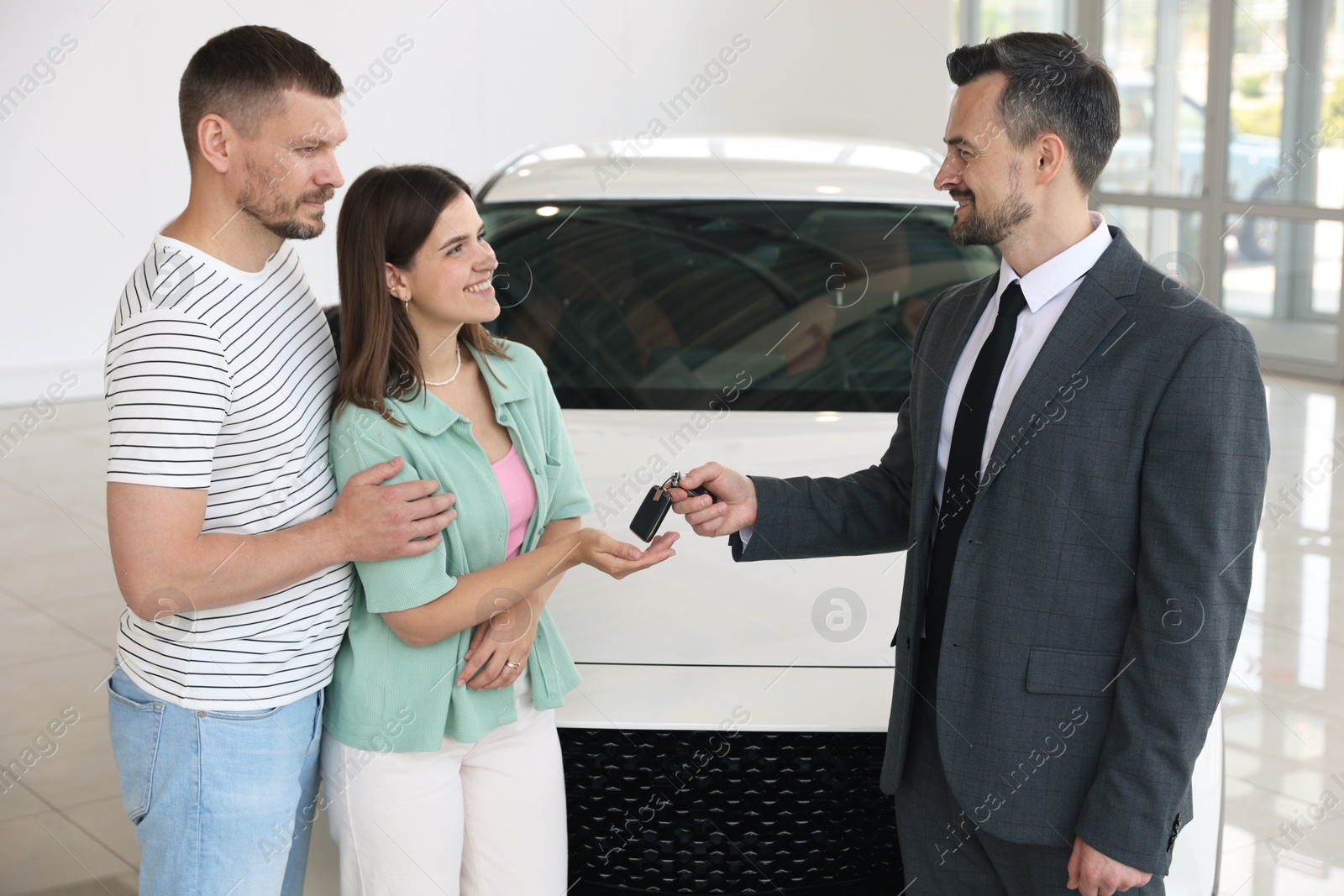 Smiling salesman giving car key to happy family in salon Photo of Smiling salesman giving car key to happy family in salon