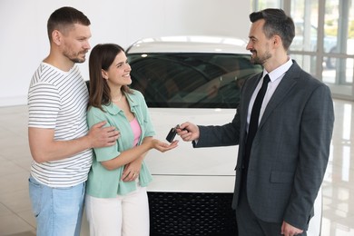 Photo of Smiling salesman giving car key to happy family in salon
