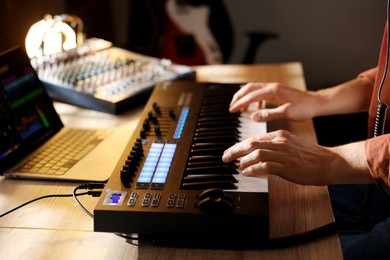 Photo of Man working with MIDI keyboard at wooden table indoors, closeup