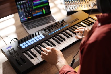 Photo of Man working with MIDI keyboard at wooden table indoors, above view