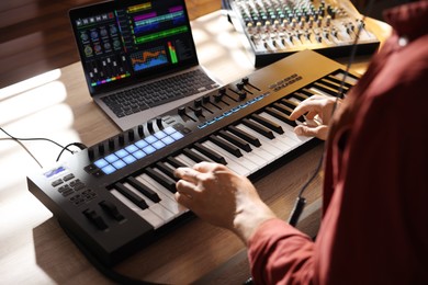 Photo of Man working with MIDI keyboard at wooden table indoors, above view
