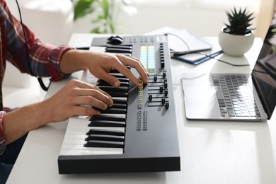 Photo of Man working with MIDI keyboard at white table indoors, closeup