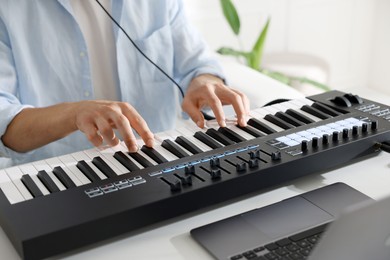 Photo of Man working with MIDI keyboard at white table indoors, closeup