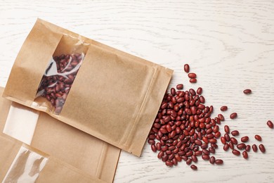 Photo of Zipper stand-up pouches and dry kidney beans on white wooden table, flat lay. Mockup for design