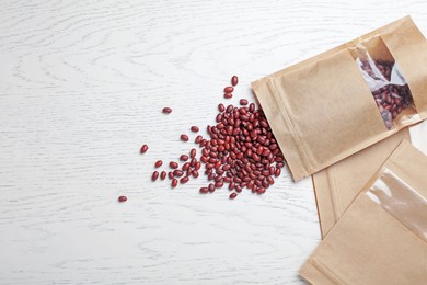 Photo of Zipper stand-up pouches and dry kidney beans on white wooden table, flat lay. Mockup for design