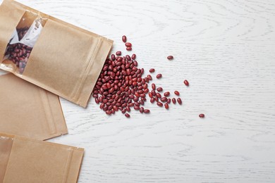Photo of Zipper stand-up pouches and dry kidney beans on white wooden table, flat lay. Mockup for design