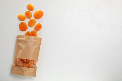 Photo of Zipper stand-up pouch with dried apricots on white table, flat lay. Mockup for design