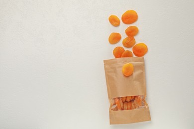 Photo of Zipper stand-up pouch with dried apricots on white table, flat lay. Mockup for design