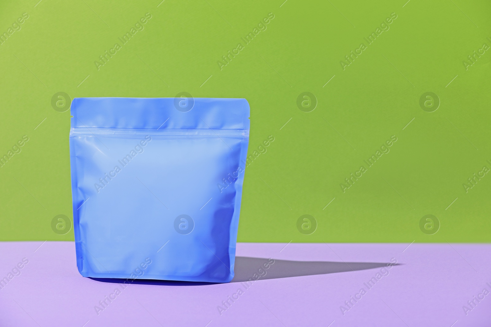 Photo of Zipper stand-up pouch on violet table against green background. Mockup for design
