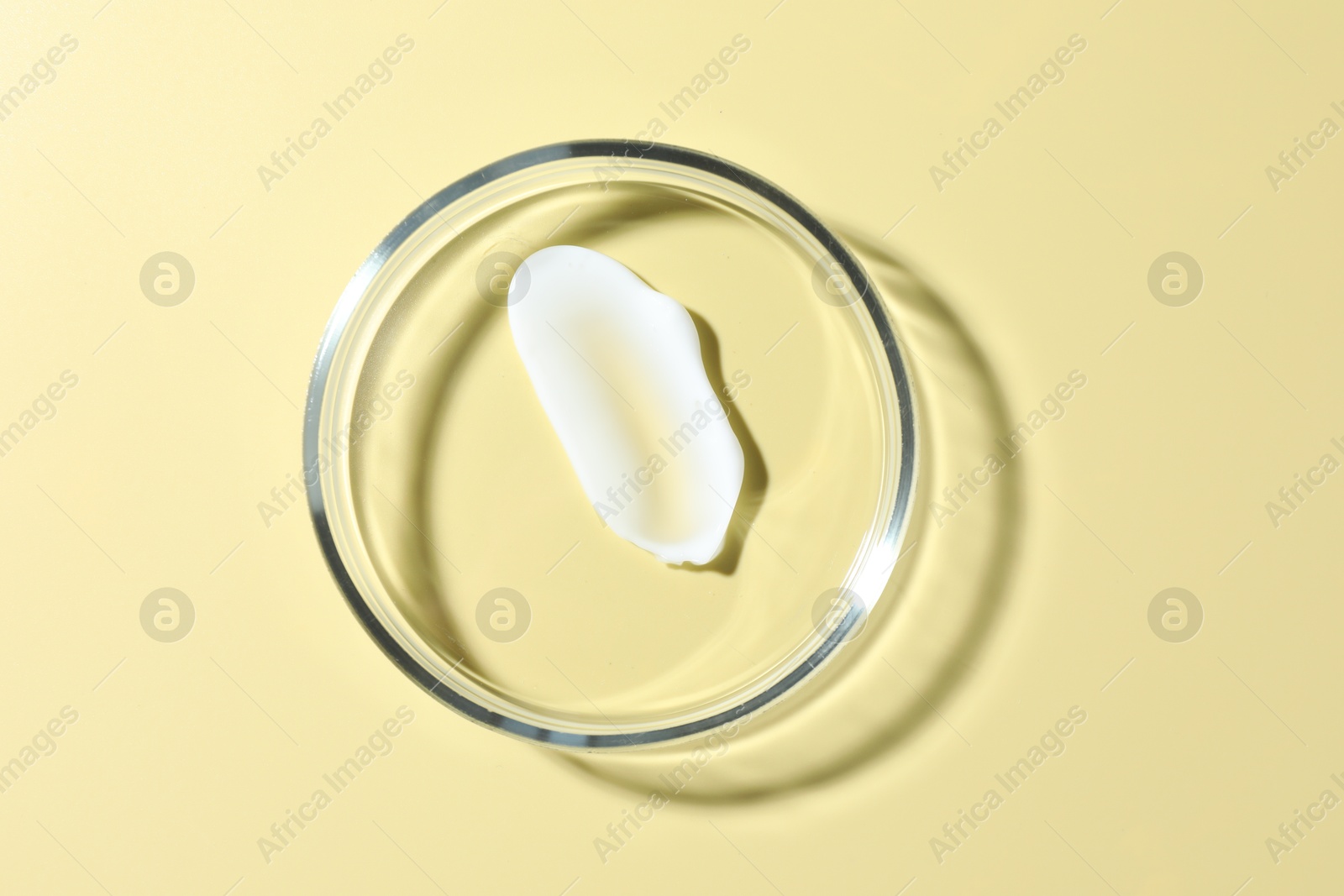 Cosmetic product in Petri dish on pale yellow background, top view Photo of Cosmetic product in Petri dish on pale yellow background, top view