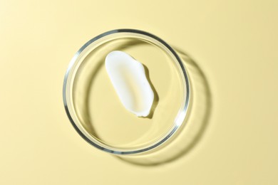Photo of Cosmetic product in Petri dish on pale yellow background, top view
