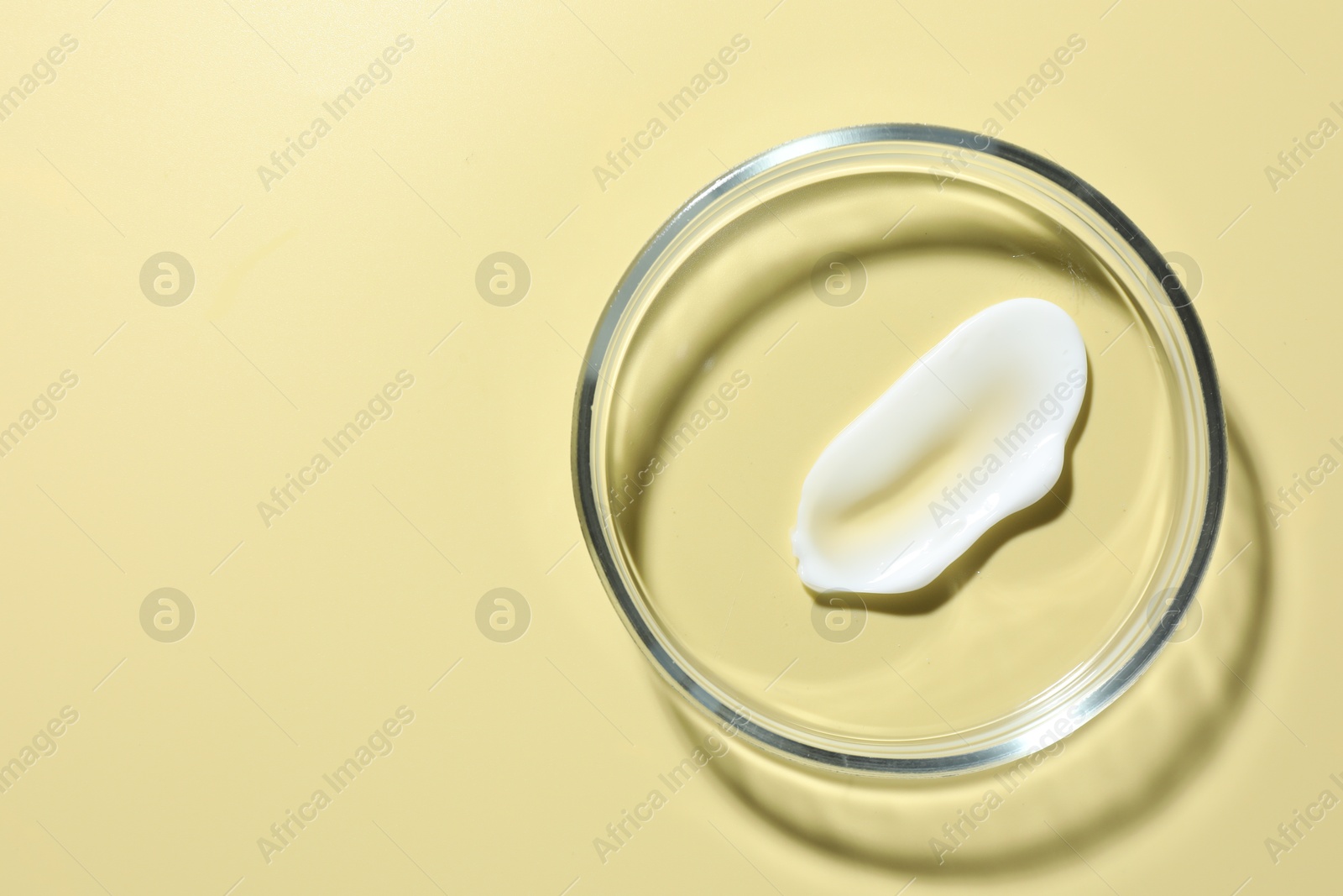 Cosmetic product in Petri dish on pale yellow background, top view. Space for text Photo of Cosmetic product in Petri dish on pale yellow background, top view. Space for text