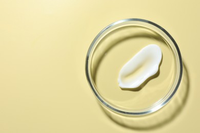 Photo of Cosmetic product in Petri dish on pale yellow background, top view. Space for text