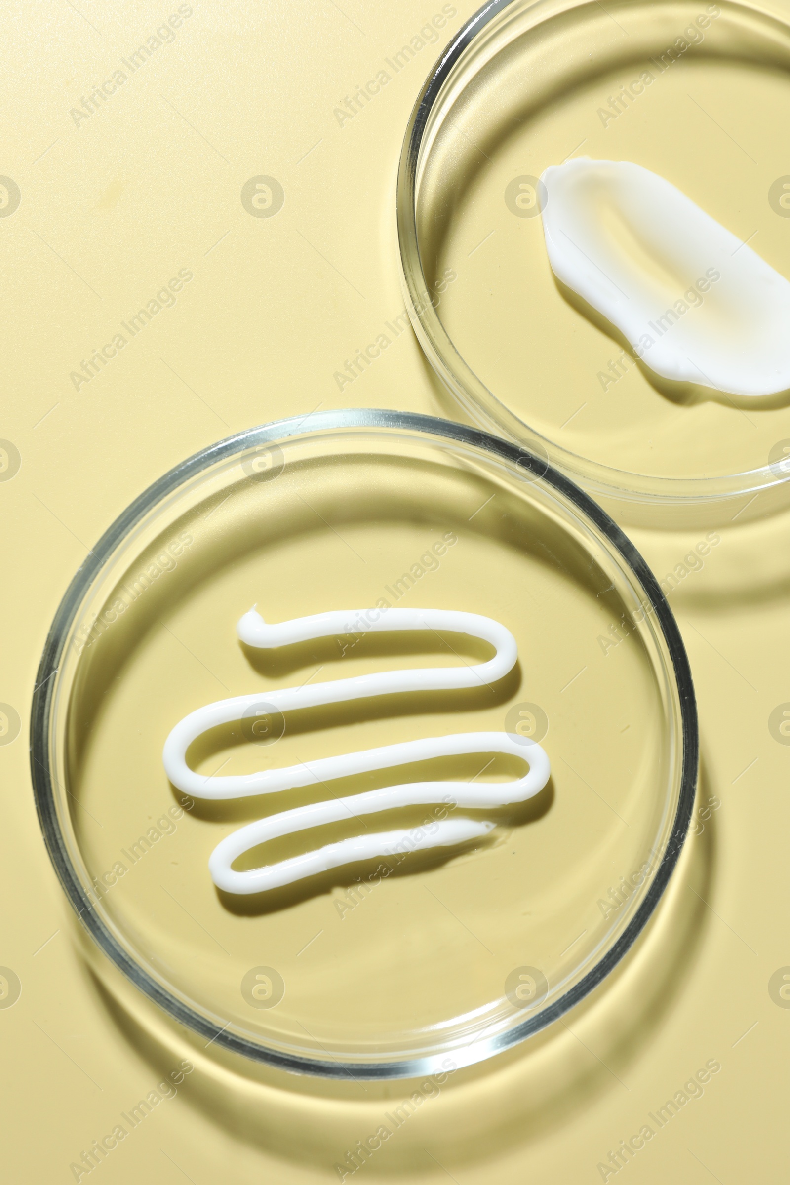 Different cosmetic products in Petri dishes on pale yellow background, flat lay Photo of Different cosmetic products in Petri dishes on pale yellow background, flat lay