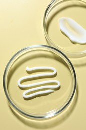 Photo of Different cosmetic products in Petri dishes on pale yellow background, flat lay