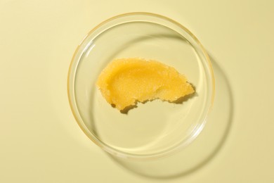 Photo of Cosmetic product in Petri dish on pale yellow background, top view