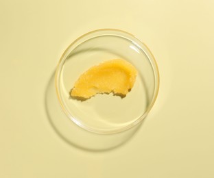 Photo of Cosmetic product in Petri dish on pale yellow background, top view