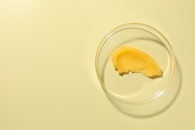 Photo of Cosmetic product in Petri dish on pale yellow background, top view. Space for text