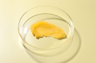 Photo of Cosmetic product in Petri dish on pale yellow background, above view
