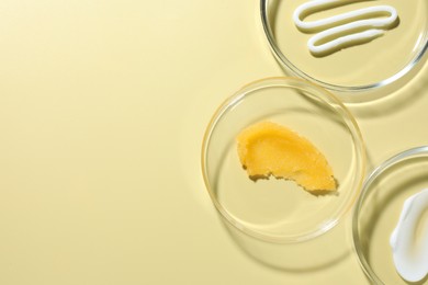 Photo of Different cosmetic products in Petri dishes on pale yellow background, flat lay. Space for text