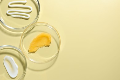 Photo of Different cosmetic products in Petri dishes on pale yellow background, flat lay. Space for text