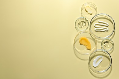 Photo of Different cosmetic products in Petri dishes on pale yellow background, flat lay. Space for text