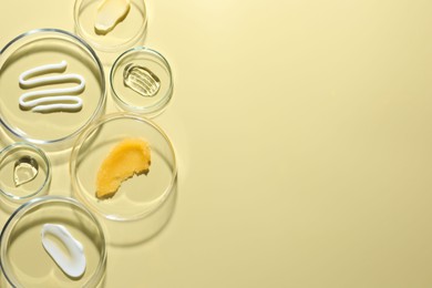 Photo of Different cosmetic products in Petri dishes on pale yellow background, flat lay. Space for text