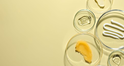 Photo of Different cosmetic products in Petri dishes on pale yellow background, flat lay. Space for text