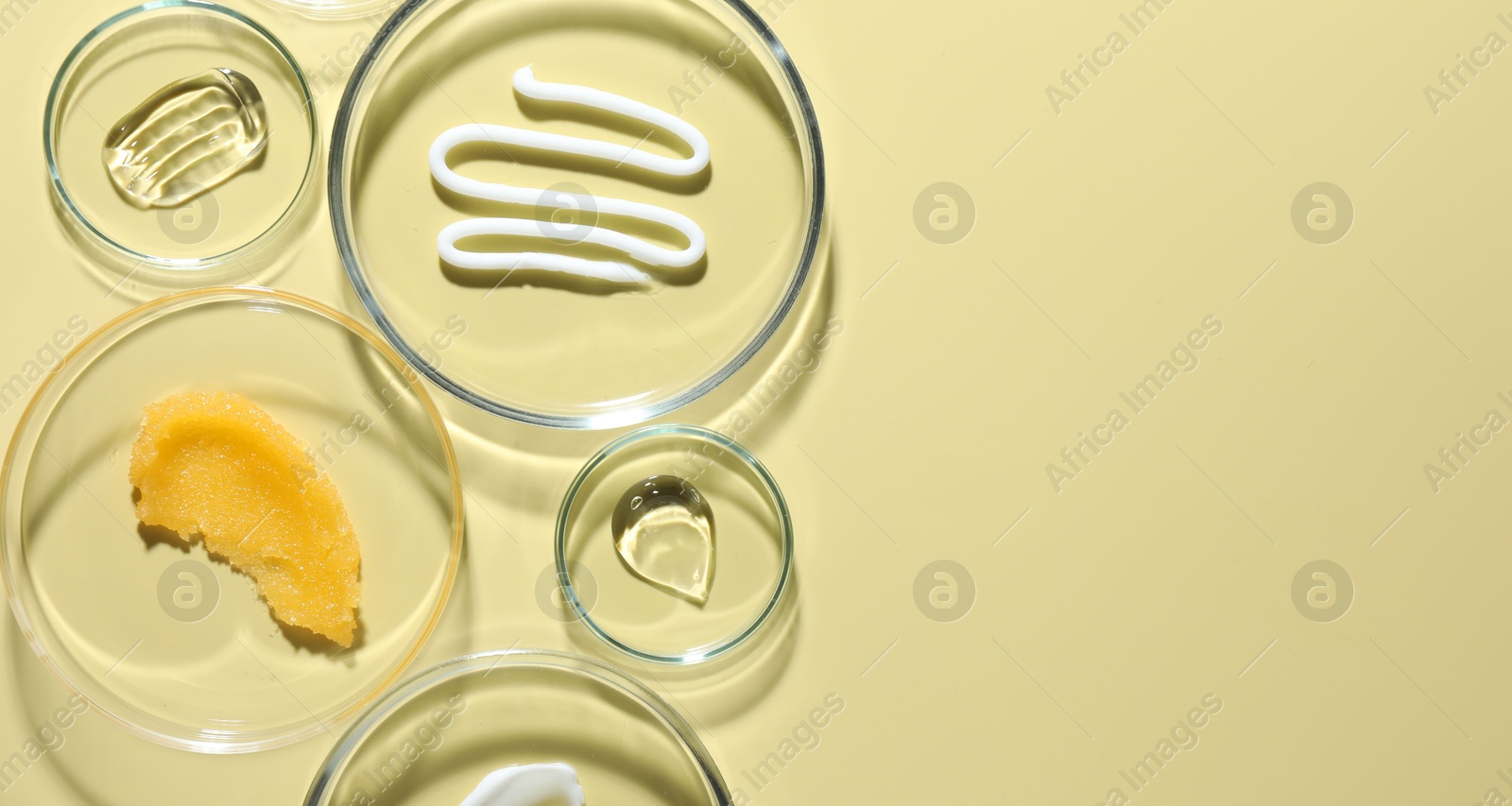 Different cosmetic products in Petri dishes on pale yellow background, flat lay. Space for text Photo of Different cosmetic products in Petri dishes on pale yellow background, flat lay. Space for text
