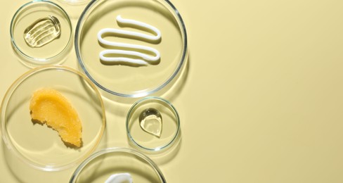 Photo of Different cosmetic products in Petri dishes on pale yellow background, flat lay. Space for text