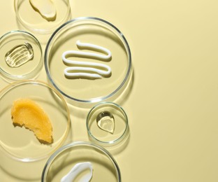 Photo of Different cosmetic products in Petri dishes on pale yellow background, flat lay. Space for text