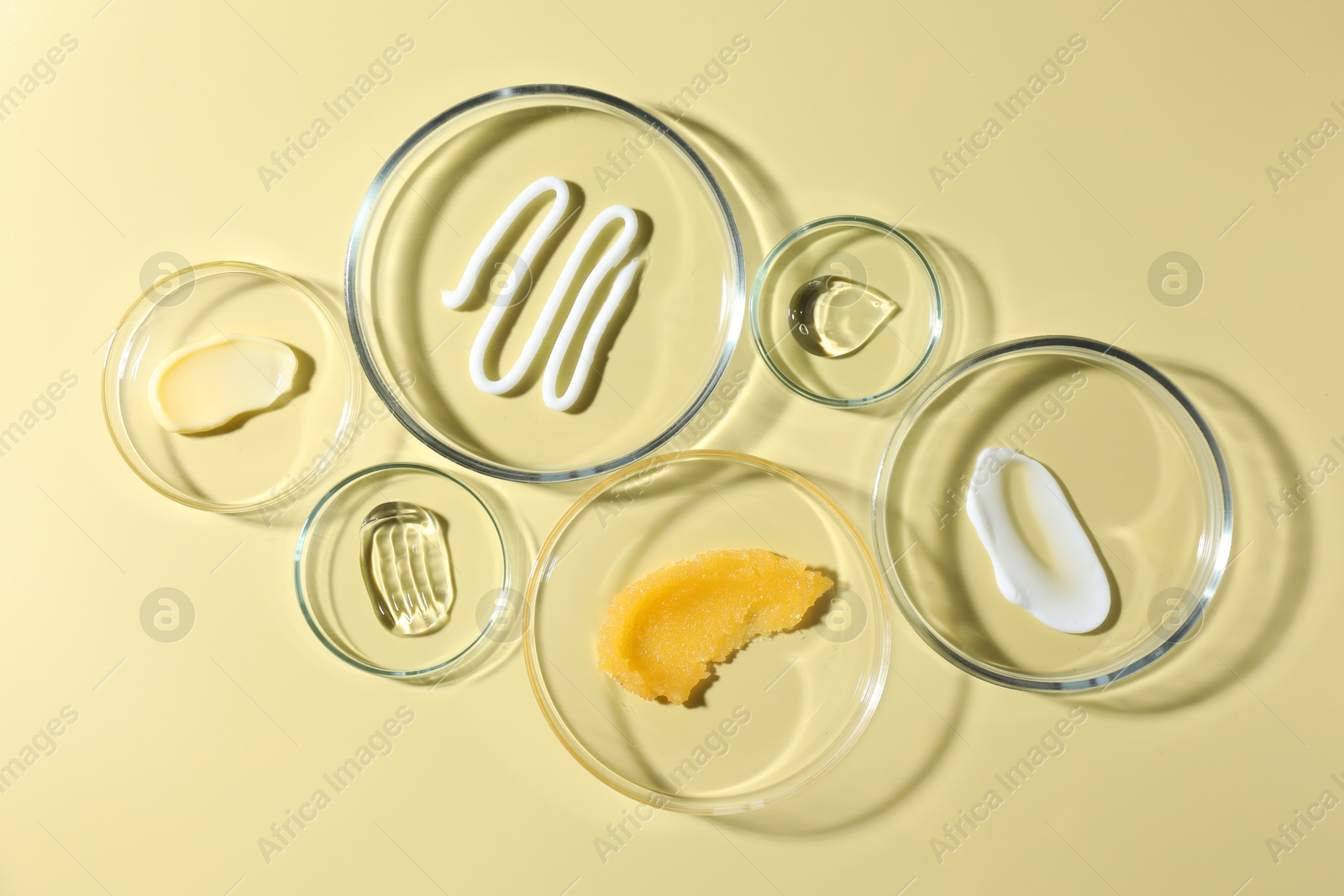 Different cosmetic products in Petri dishes on pale yellow background, flat lay Photo of Different cosmetic products in Petri dishes on pale yellow background, flat lay
