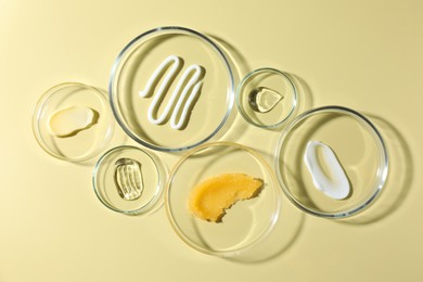 Photo of Different cosmetic products in Petri dishes on pale yellow background, flat lay