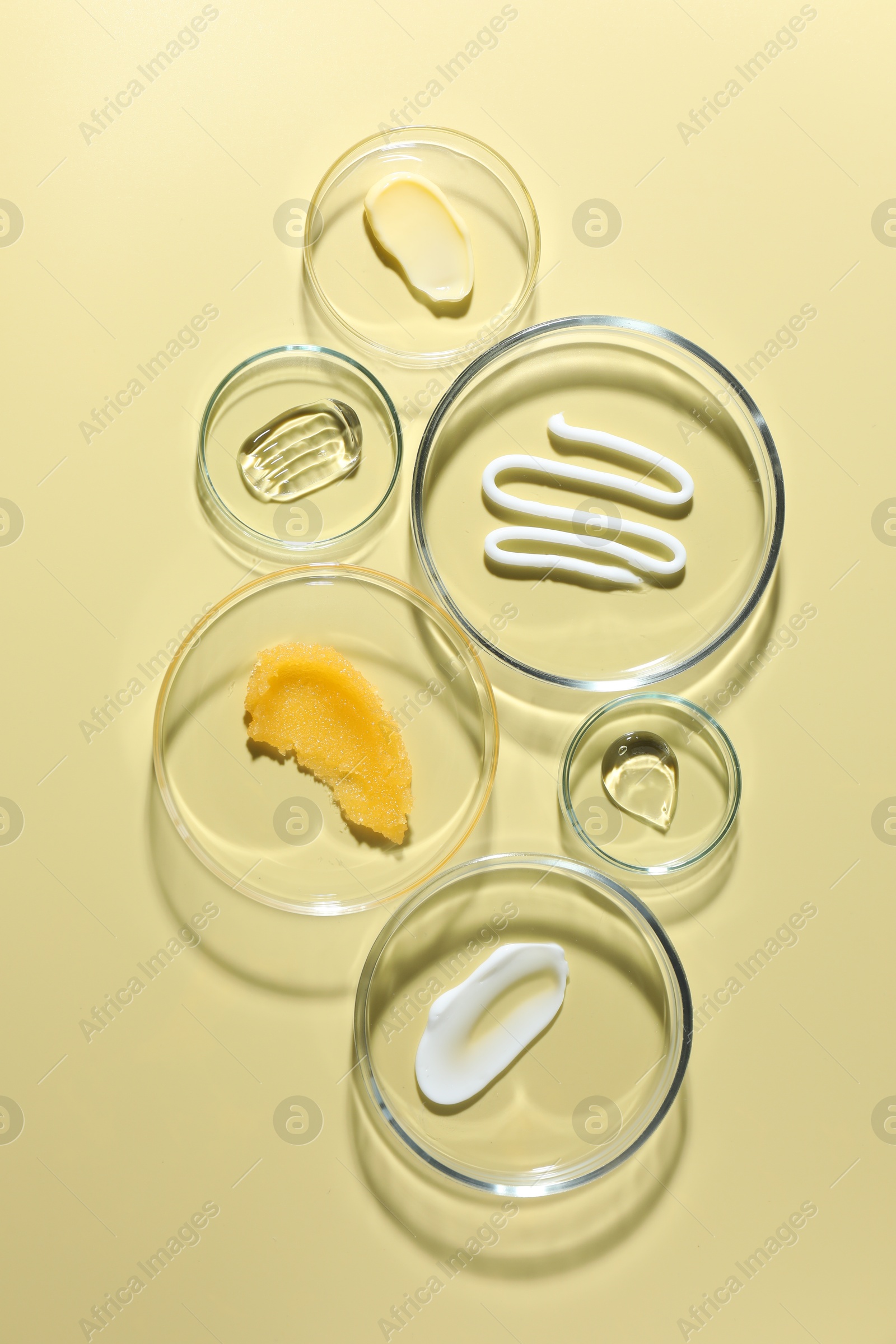 Different cosmetic products in Petri dishes on pale yellow background, flat lay Photo of Different cosmetic products in Petri dishes on pale yellow background, flat lay