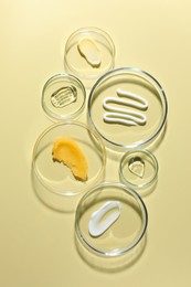 Photo of Different cosmetic products in Petri dishes on pale yellow background, flat lay