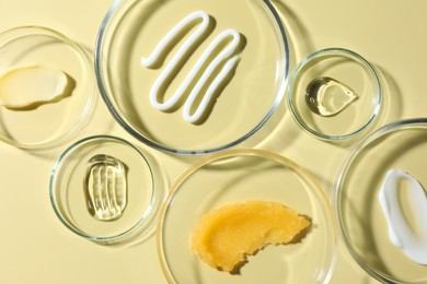 Photo of Different cosmetic products in Petri dishes on pale yellow background, flat lay