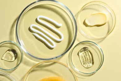Photo of Different cosmetic products in Petri dishes on pale yellow background, flat lay