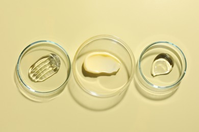 Photo of Different cosmetic products in Petri dishes on pale yellow background, flat lay